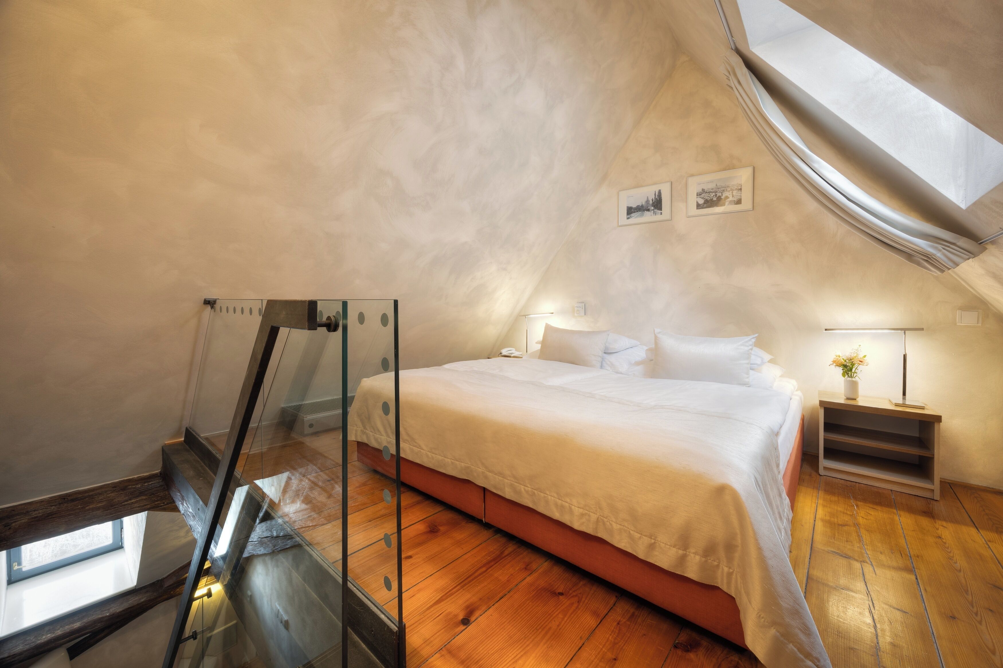 Un dormitorio con techo inclinado, una cama, una mesita de noche, una lámpara y una ventana.