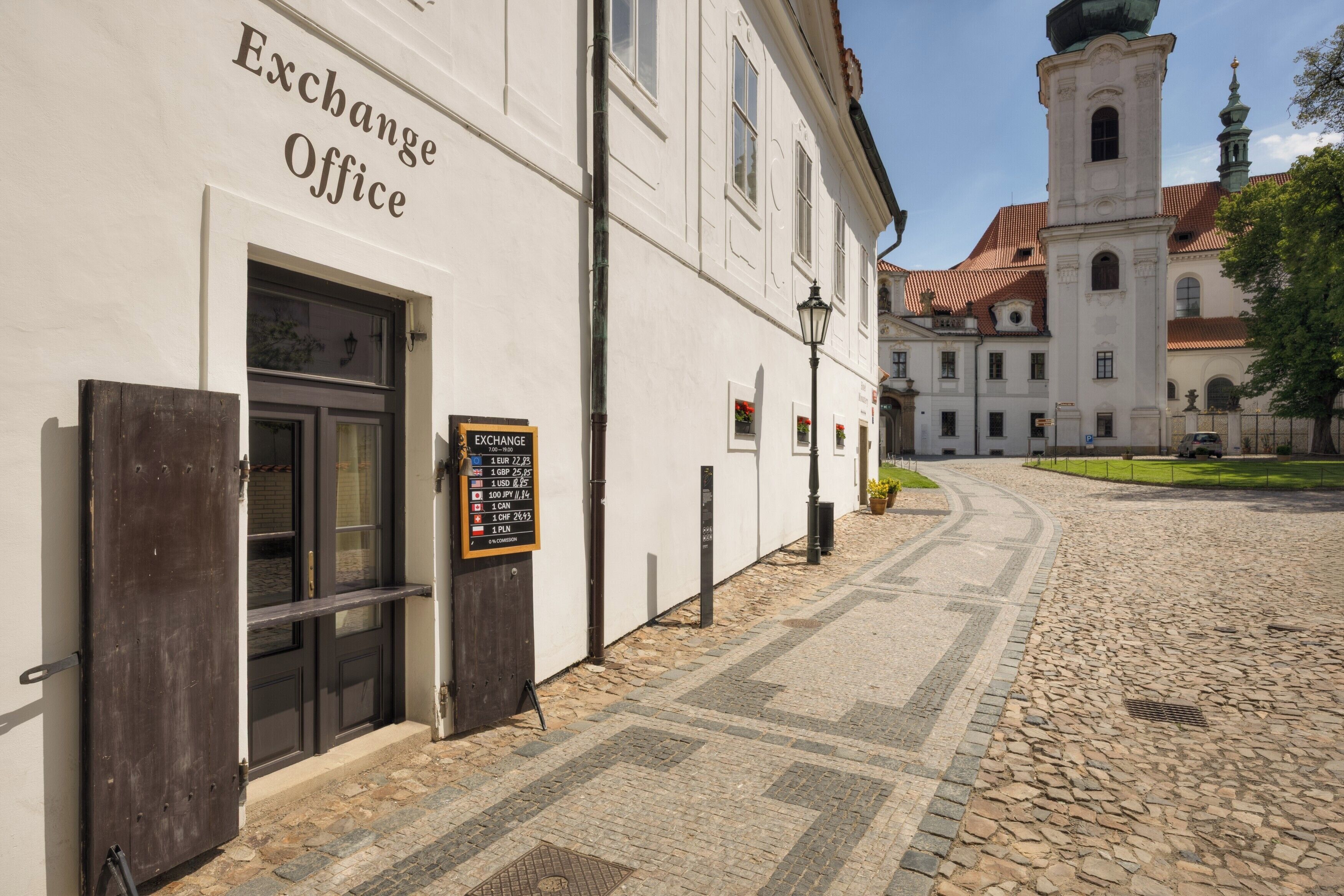 Un bâtiment portant l’inscription « Bureau de change », situé dans une rue pavée, avec un lampadaire et une tour en arrière-plan.