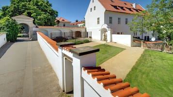 A white building with a red-tiled roof, a paved courtyard, and a stone wall with a gate.
