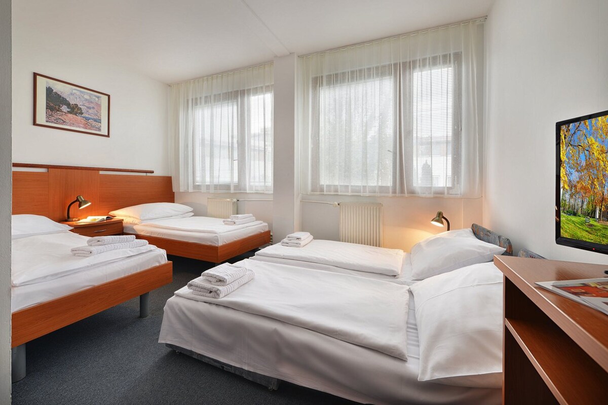 A hotel room with three beds, a desk, a TV, and a painting on the wall.