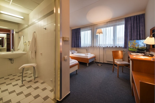 A hotel room with a bathroom, two beds, a desk, and a TV.