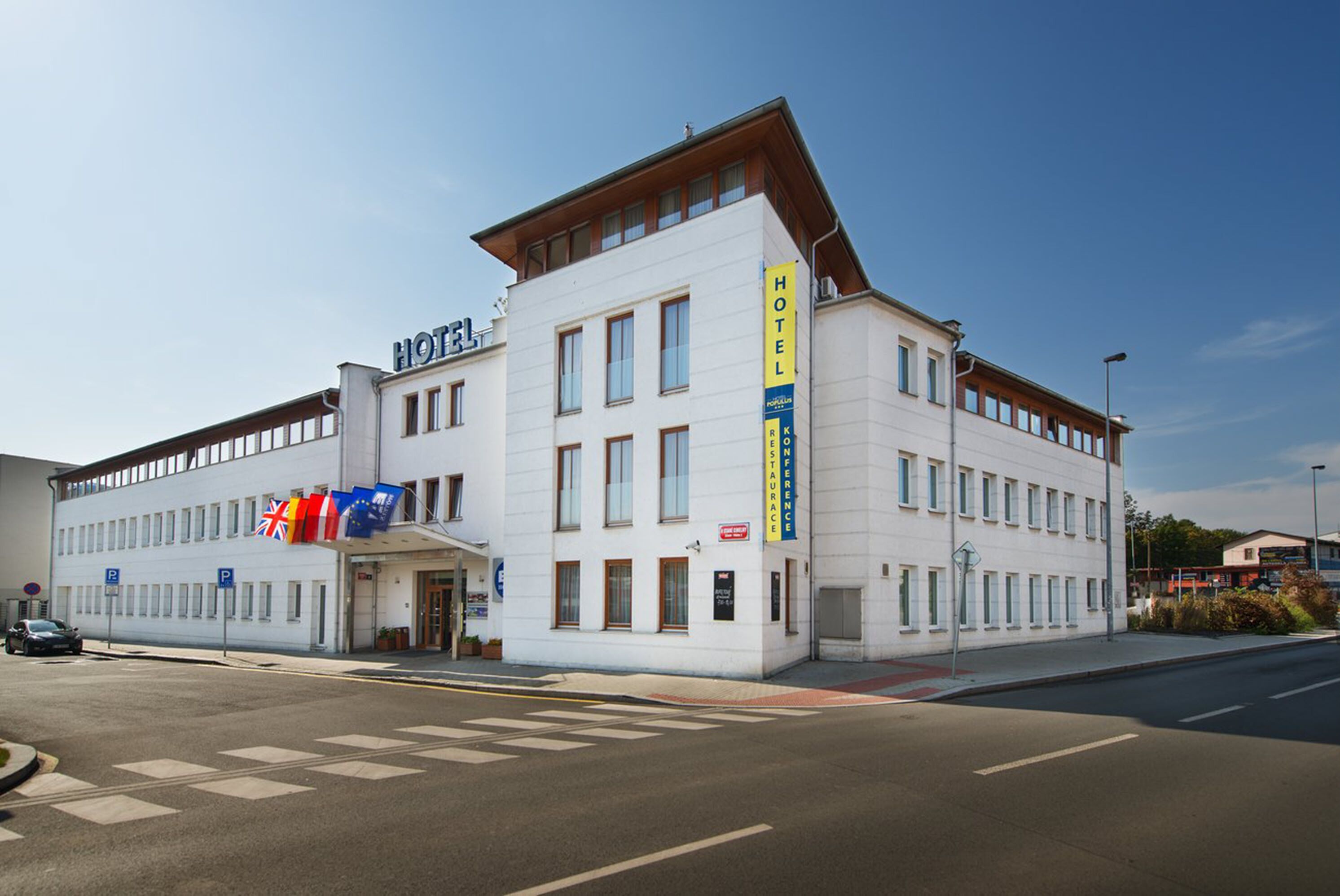 A white hotel with multiple floors, a prominent 'HOTEL' sign, and several flags including the UK flag.