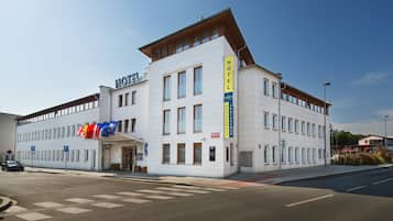 A white hotel with multiple floors, a prominent 'HOTEL' sign, and several flags including the UK flag.