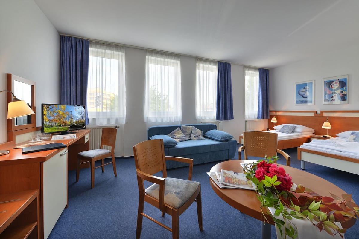 Quarto de hotel com escrivaninha, cadeira, cama e sofá.