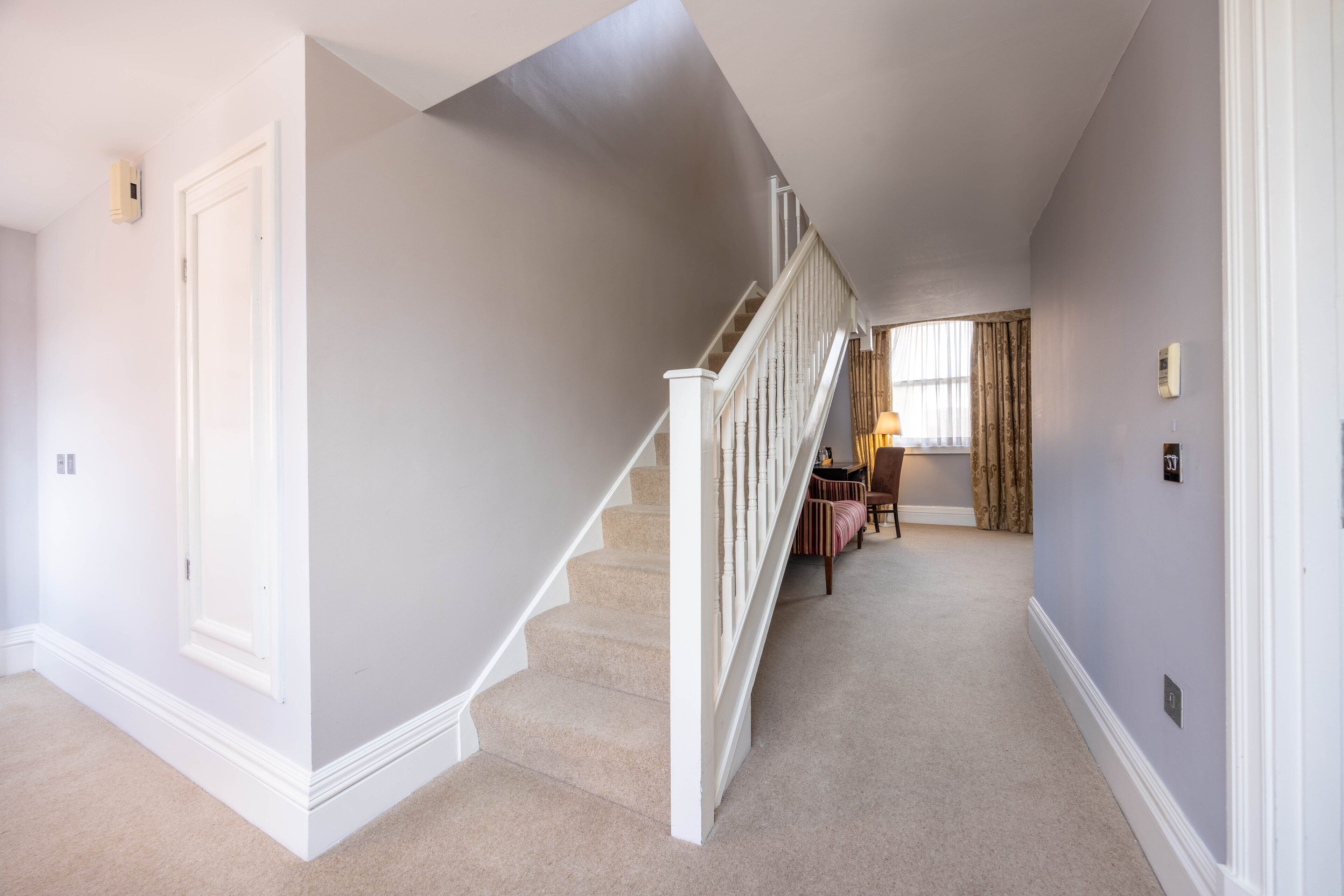 A hallway with a carpeted staircase, a door, and a window with curtains.