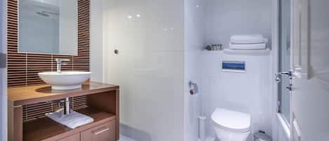 Un baño moderno con tocador de madera, un espejo grande, un lavabo blanco, un inodoro y una zona de ducha.