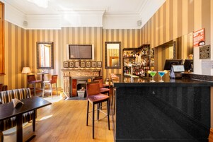 Una zona de bar con mostrador de mármol negro, revestimiento de papel tapiz a rayas y una chimenea.