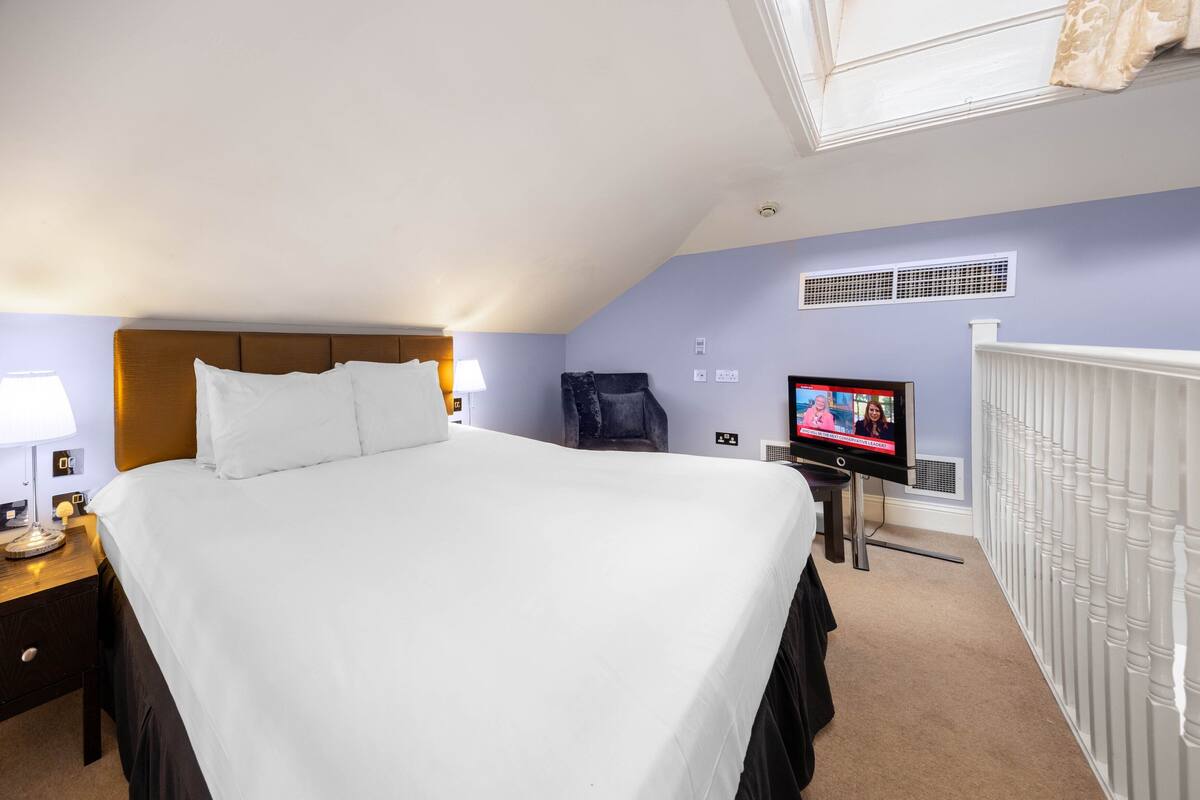 A hotel room with a large bed, a TV, a chair, and a radiator.
