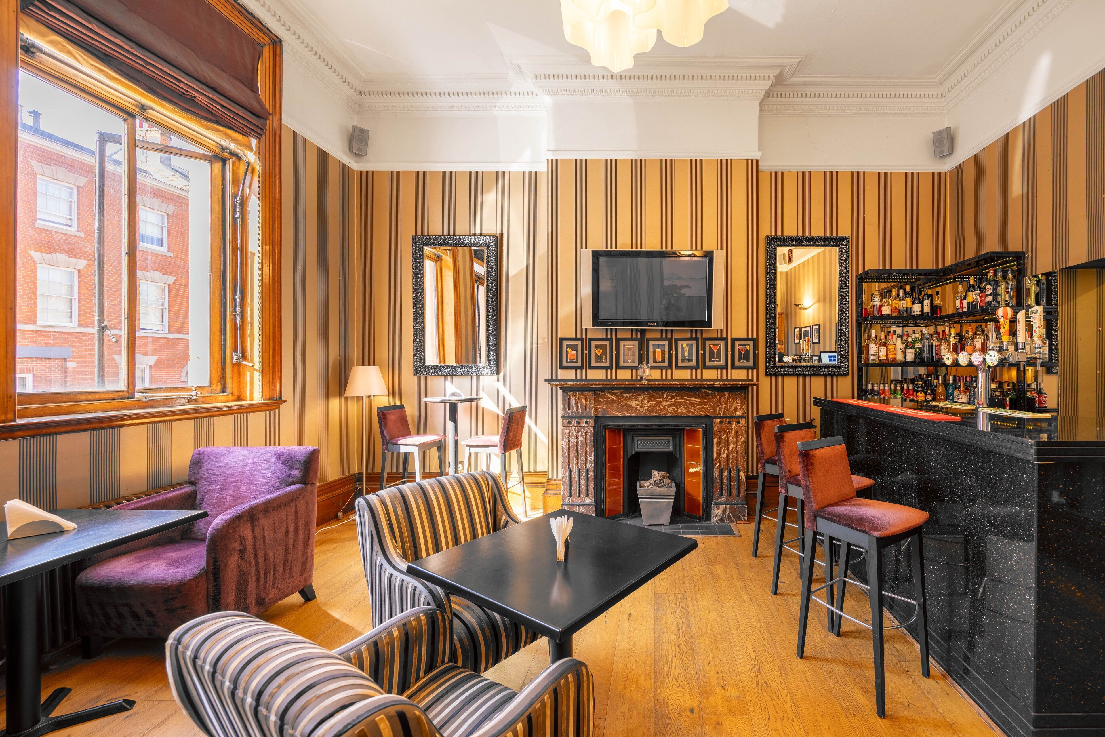 A bar area with striped wallpaper, a fireplace, and a television mounted on the wall.