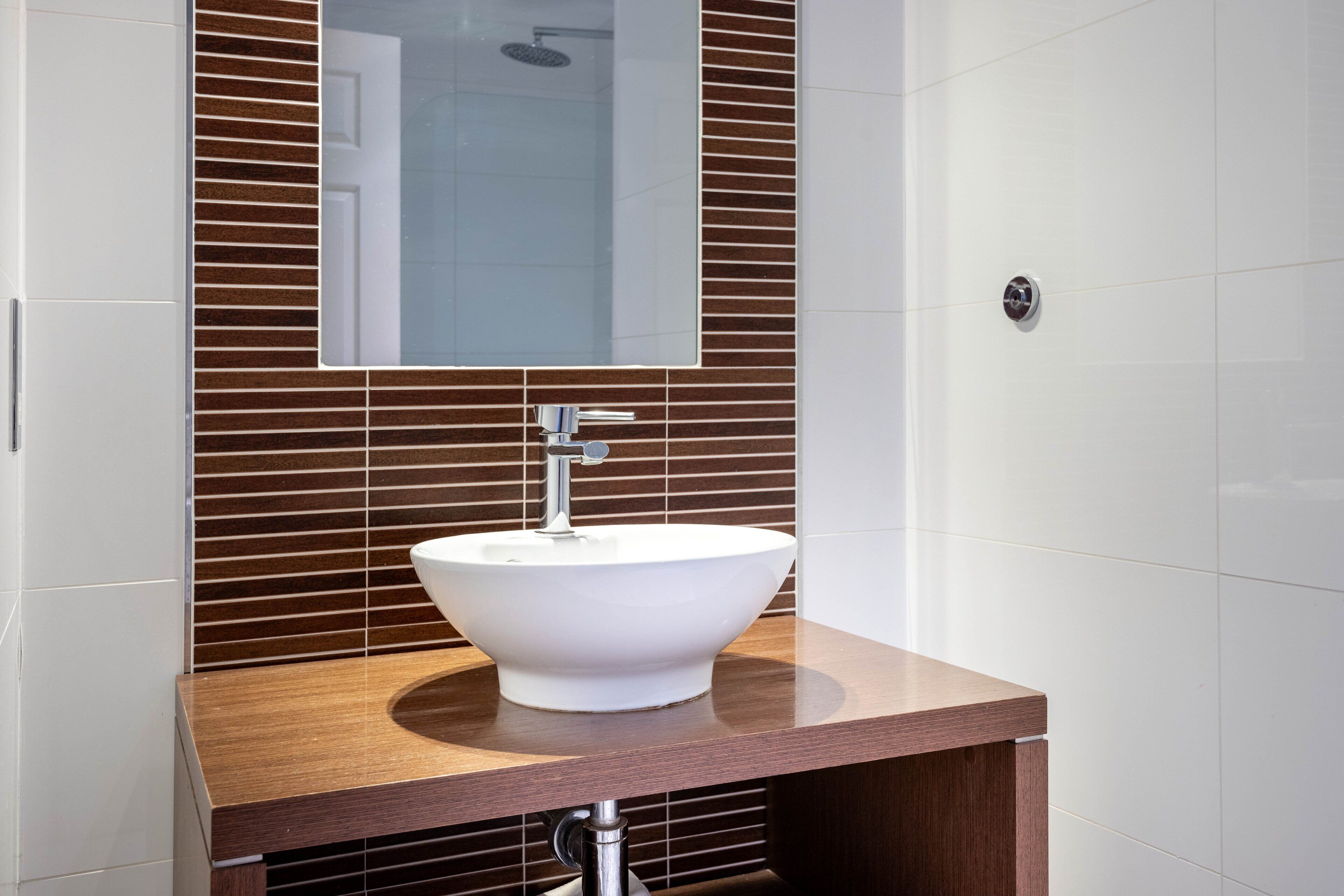 A bathroom with a white sink, wooden vanity, and a mirror above the sink.