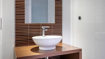 A bathroom with a white sink, wooden vanity, and a mirror above the sink.