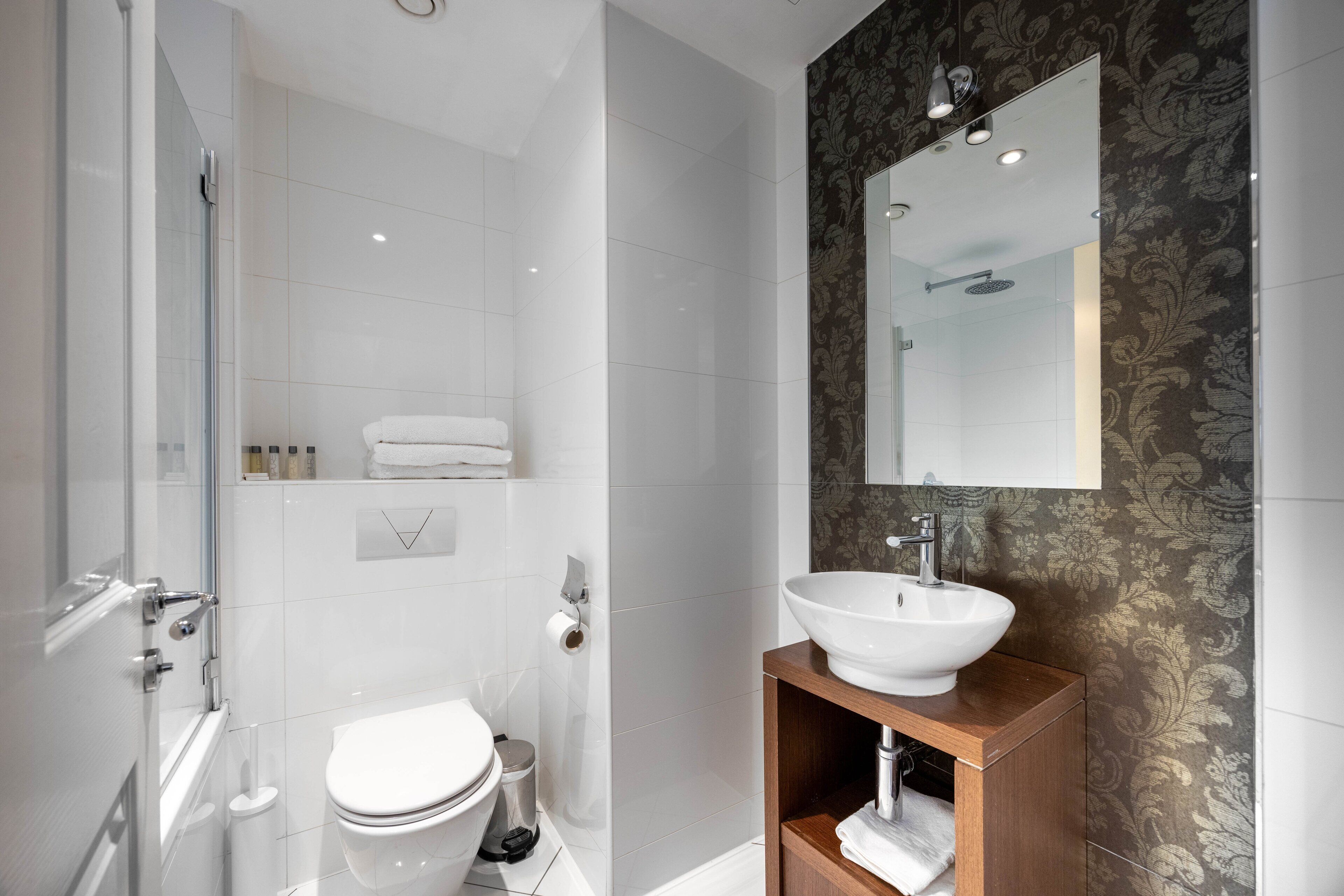 Une salle de bain moderne avec une douche à parois de verre, des toilettes blanches et un meuble-lavabo en bois avec un lavabo blanc.