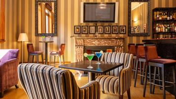 A bar area with striped upholstered chairs, a television above the fireplace, and framed pictures on the wall.