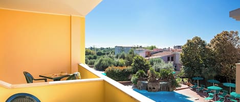 A balcony with a view of a swimming pool and greenery, featuring a table and chairs.
