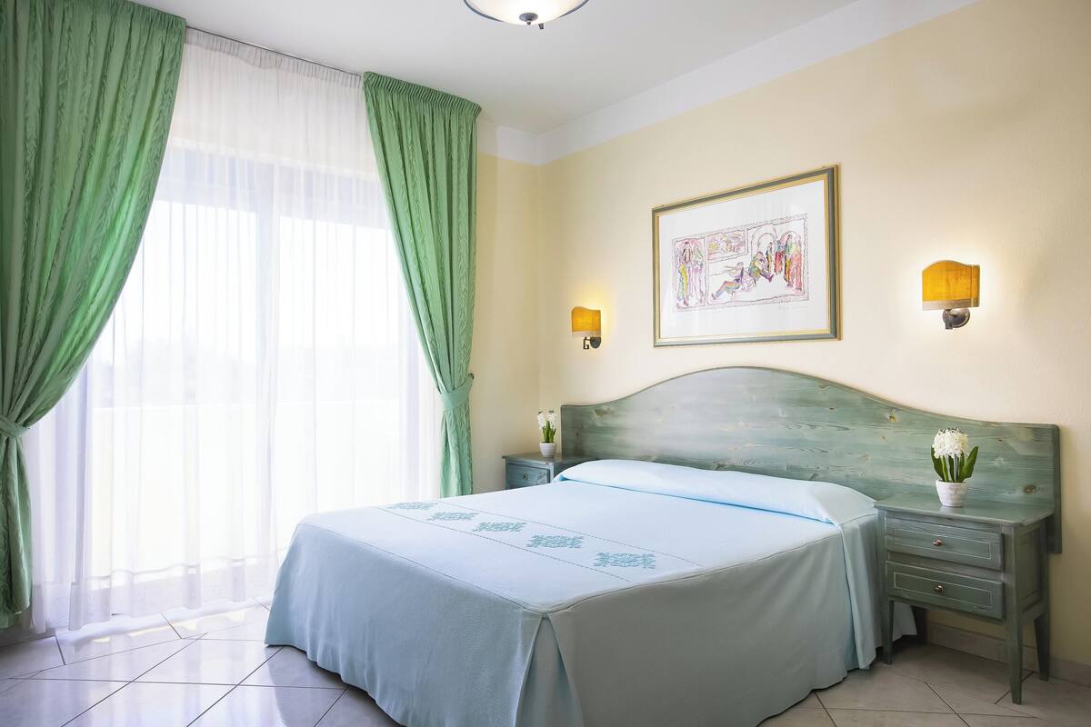 A neatly arranged bedroom with a bed, two bedside tables, a wall-mounted lamp, and a framed picture.