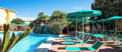A pool area with lounge chairs and umbrellas, surrounded by greenery and a building.