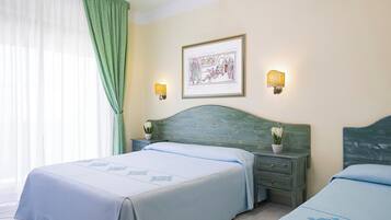 A hotel room with two beds, a green headboard, a framed picture on the wall, and two wall-mounted lamps.
