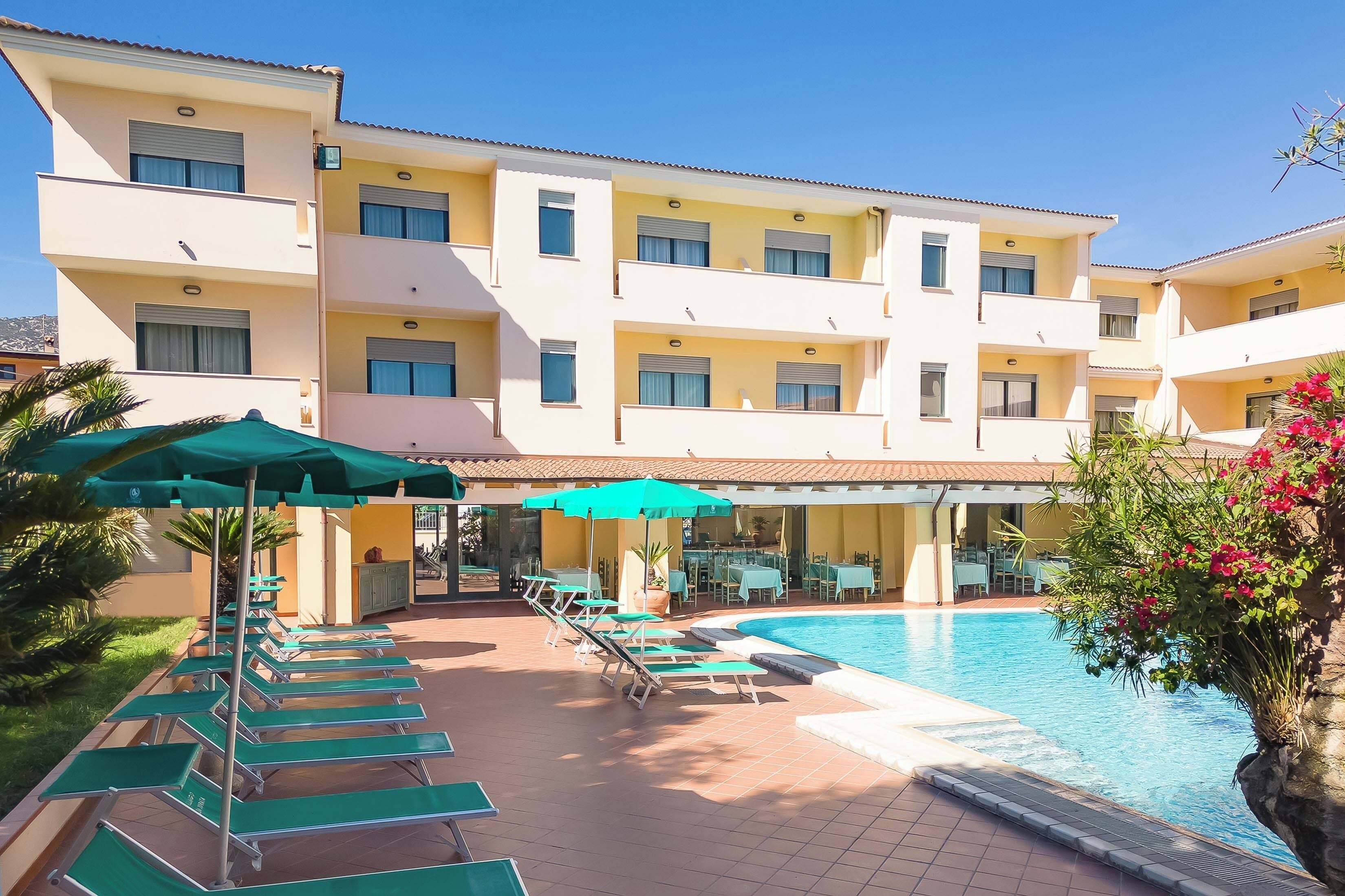 A hotel with a swimming pool, sun loungers, and outdoor seating.