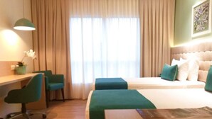 Una habitación de hotel con una cama, dos sillas, un escritorio y una ventana con cortinas.