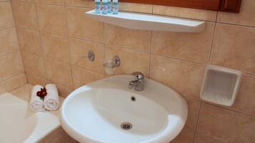 A bathroom with a white sink, a mirror above it, and a shelf with toiletries.