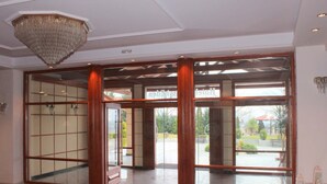 A hotel lobby with a red carpet, wooden columns, and large glass doors leading outside. - Famissi Eden Hotel (Kalabaka)