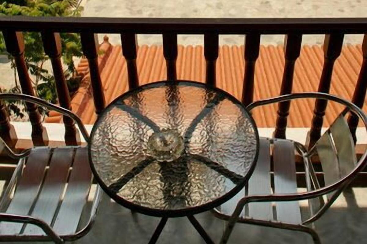 A balcony with a glass table and chairs, overlooking a swimming pool and a grassy area with lounge chairs and umbrellas.