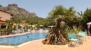 A swimming pool with lounge chairs and umbrellas, surrounded by greenery and a mountain backdrop. - Famissi Eden Hotel (Kalabaka)