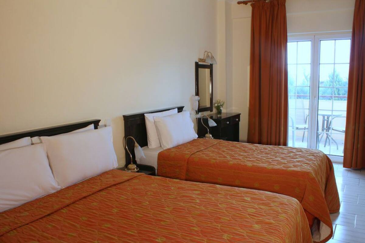 A hotel room with two beds, a nightstand, a mirror, and a view of the outside.