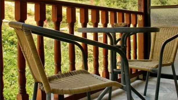 A balcony with two wicker chairs and a wooden railing overlooking a mountainous landscape. - Famissi Eden Hotel (Kalabaka)
