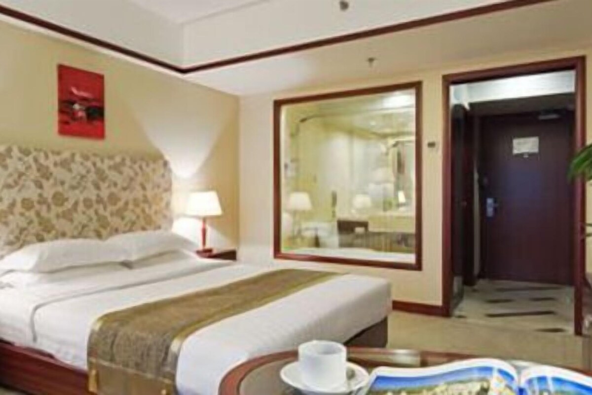 A hotel room with a large bed, two bedside tables with lamps, a mirror, and a door leading to another room.