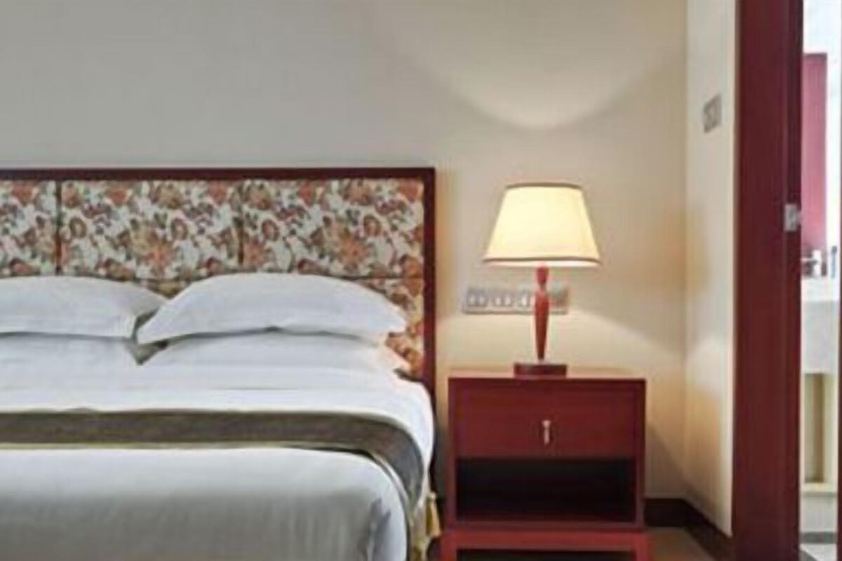 A hotel room with a bed, a nightstand with a lamp, and a door.