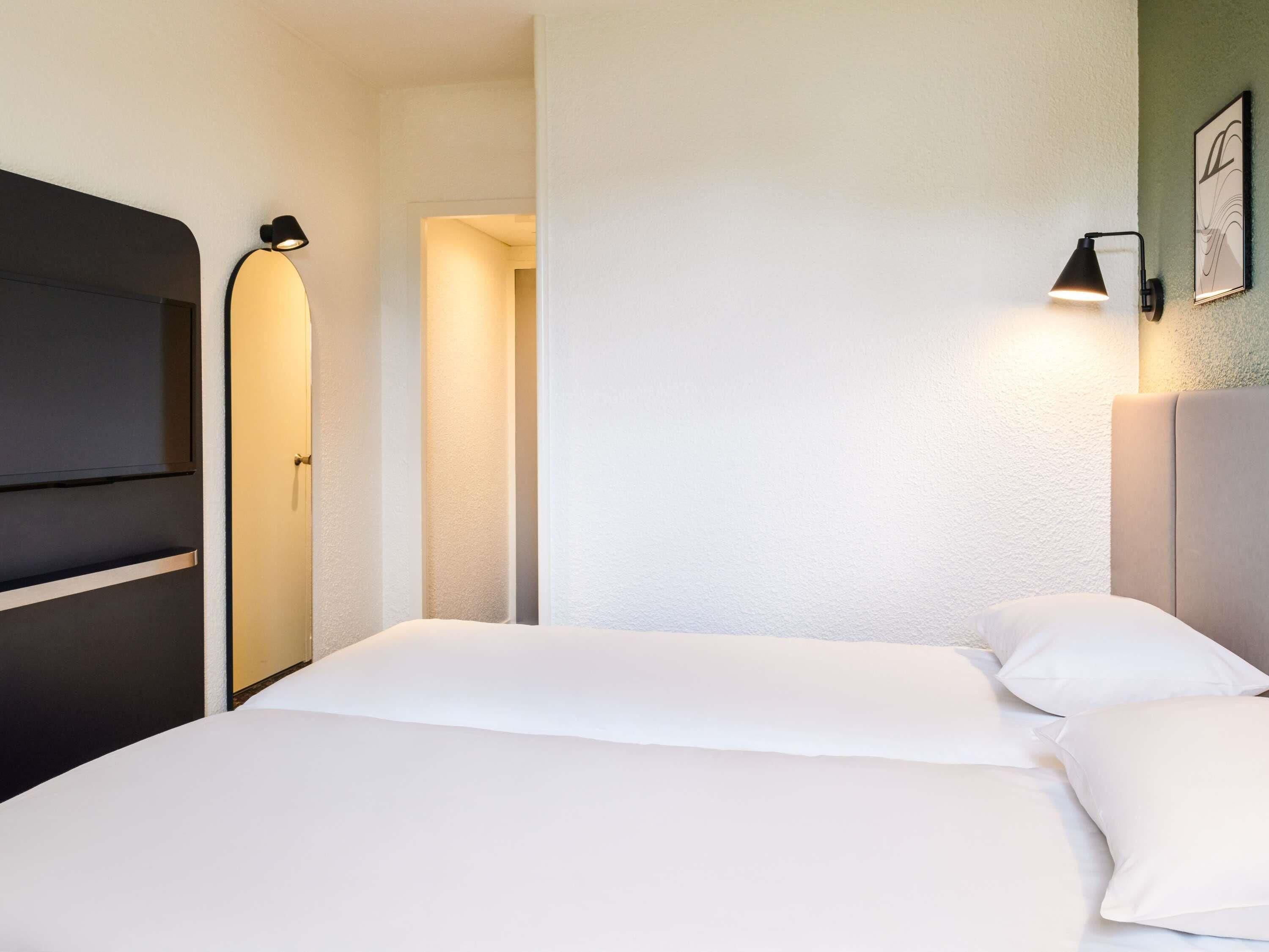 A hotel room with a bed, two bedside lamps, a door, and a framed picture on the wall.
