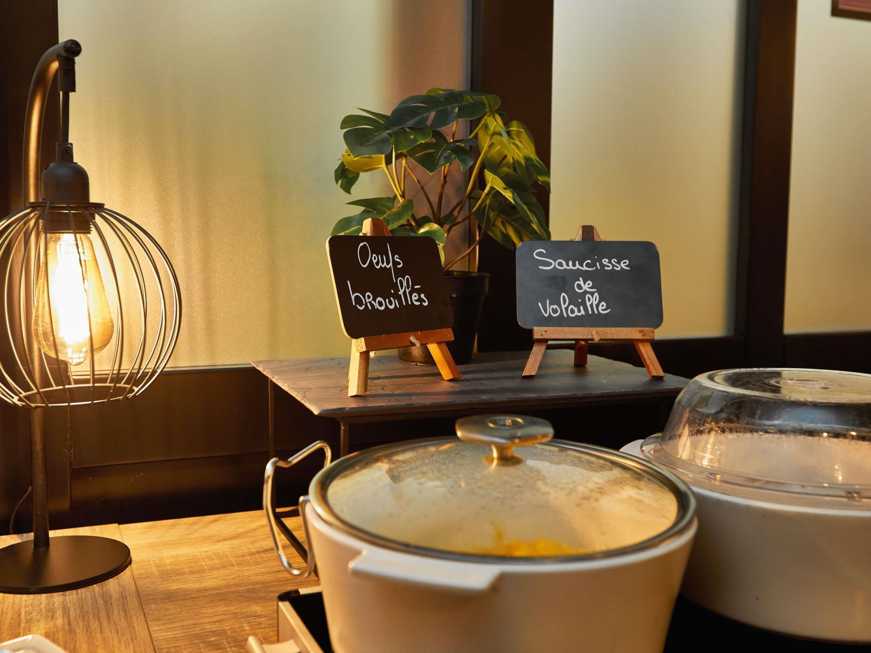 Taula amb una olla de sopa, un cartell que indica 'Saucisse de Vopaille' i un altre amb 'Oeufs brouilles'.
