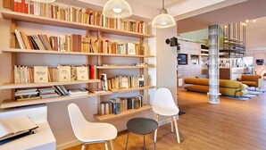 A modern living room with wooden bookshelves, white chairs, and a central column. - ibis La Roche sur Yon (Mouilleron-le-Captif)