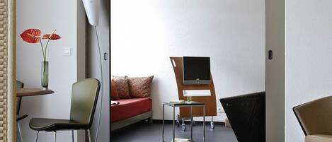 A modern room with a sofa, a chair, a desk, a flat-screen TV, and a vase with flowers.
