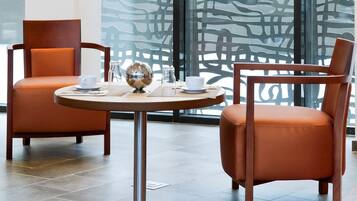 A modern hotel room with two leather armchairs, a round table with a metallic base, and a decorative glass object.