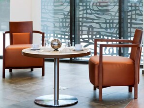 Ein modernes Hotelzimmer mit zwei Ledersesseln, einem runden Tisch mit Metallfuß und einem dekorativen Glasobjekt.