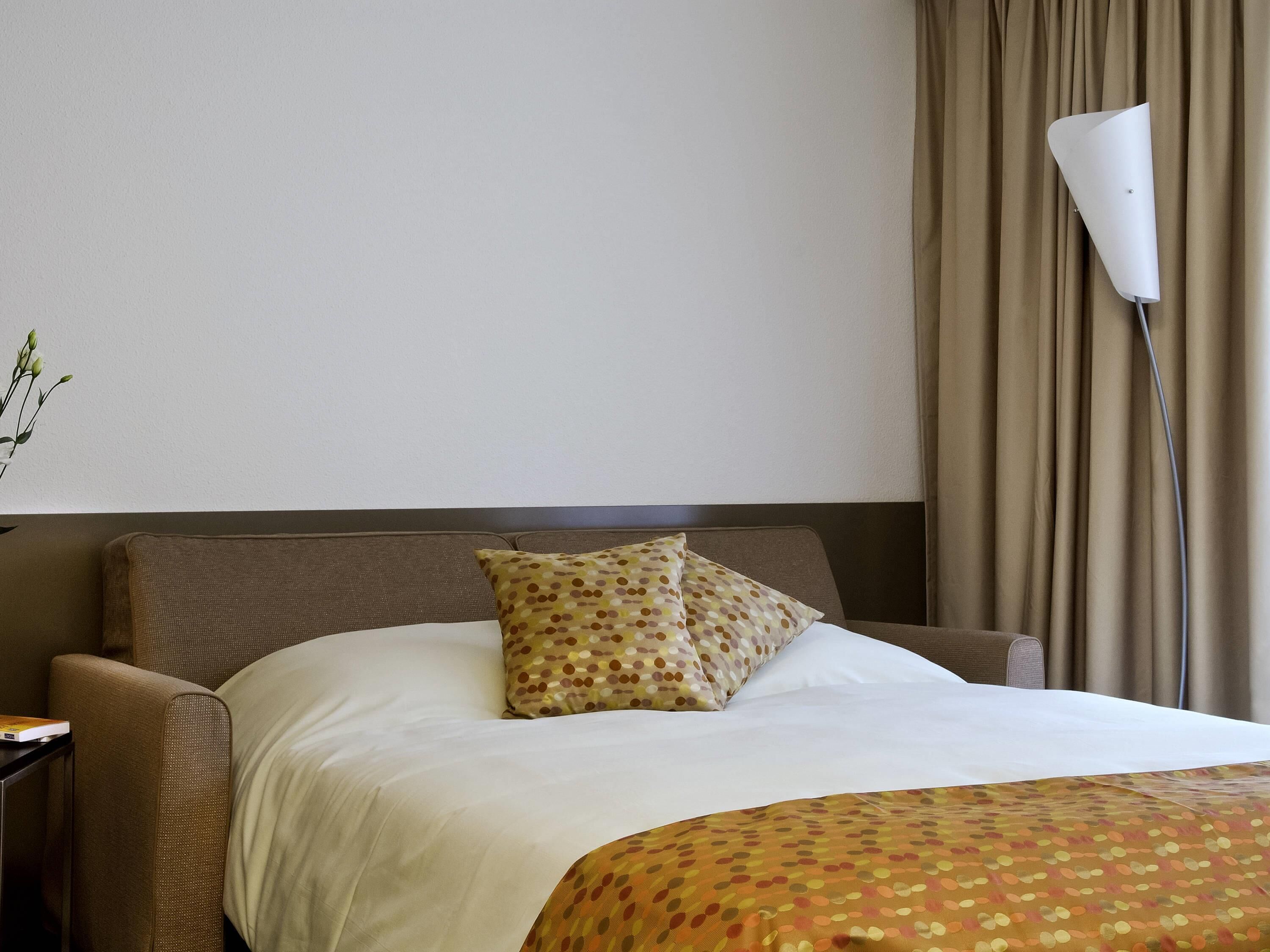 A hotel room with a bed, a nightstand, a lamp, and a window with curtains.