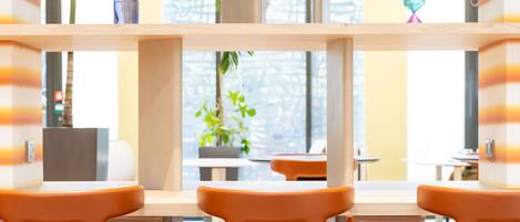 Un espacio interior moderno con mesas y sillas de madera, plantas en macetas y vistas a través de amplios ventanales.