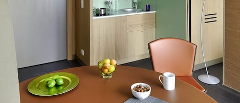 Un coin repas avec une table dressée pour deux personnes, un saladier de fruits, une assiette avec une demi-pomme et une tasse.