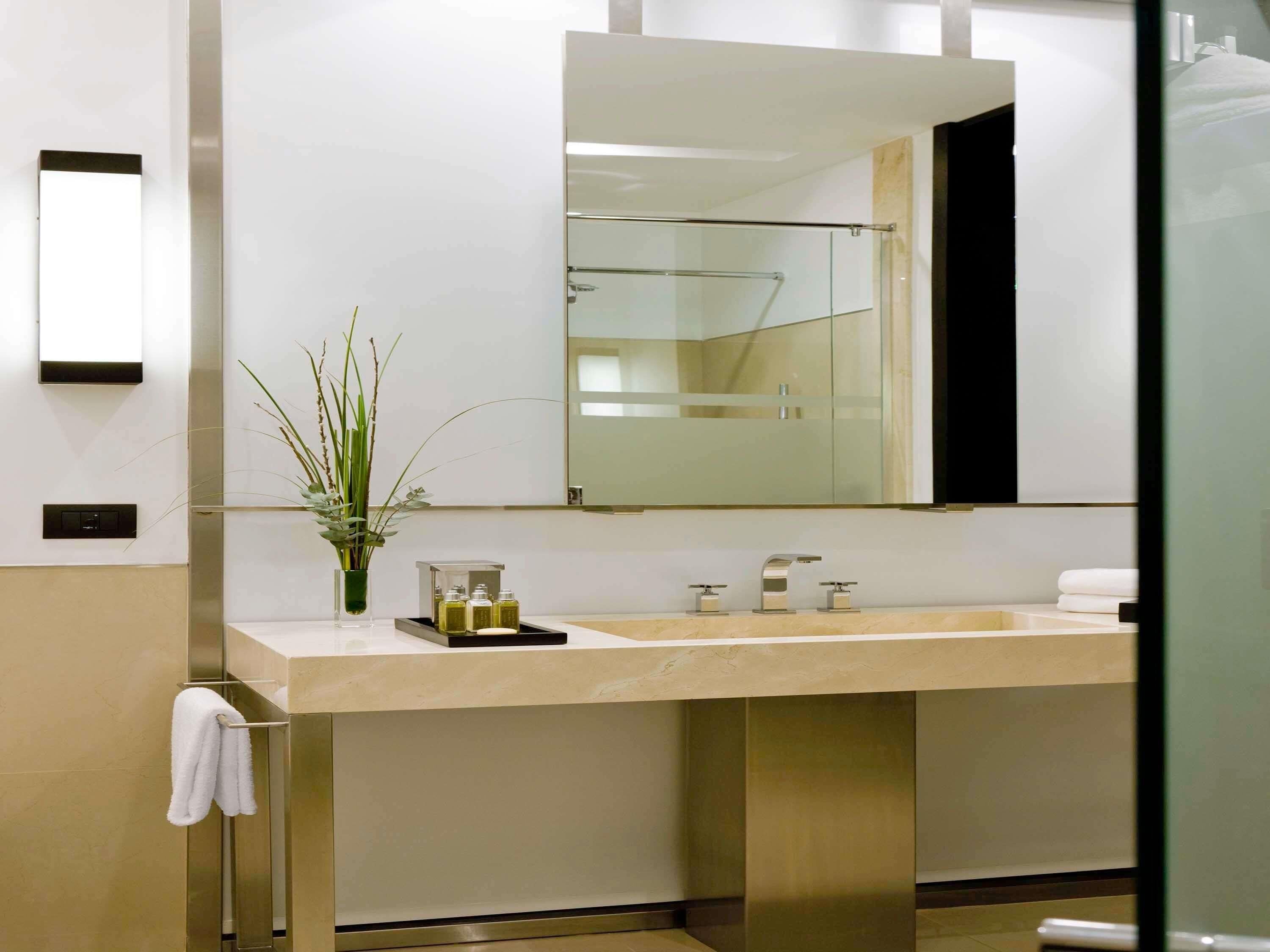 A modern bathroom with a large mirror, a sink with two faucets, and a towel rack.