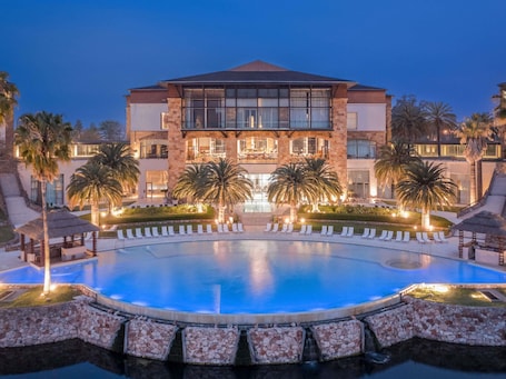 A large hotel with a swimming pool, palm trees, and a well-lit entrance.. Sofitel La Reserva Cardales