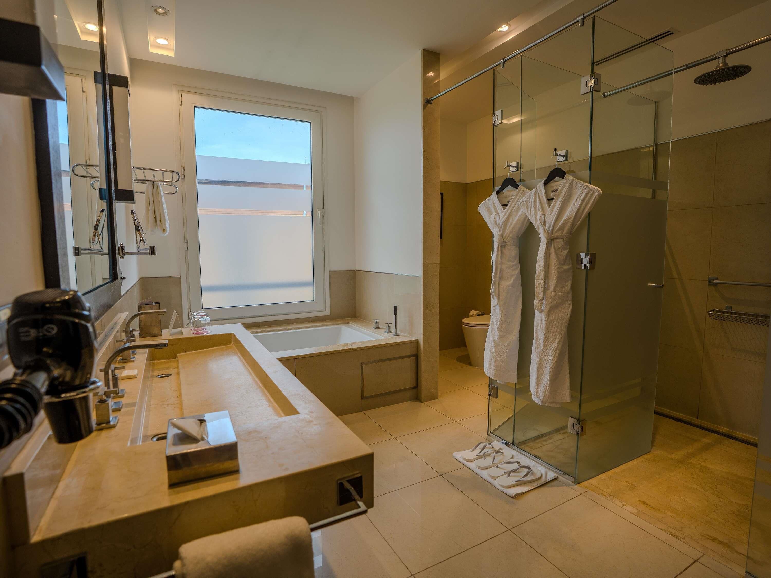 Un baño moderno con un espejo grande, una bañera, una ducha con mampara de vidrio y un tocador con lavamanos y perchero.