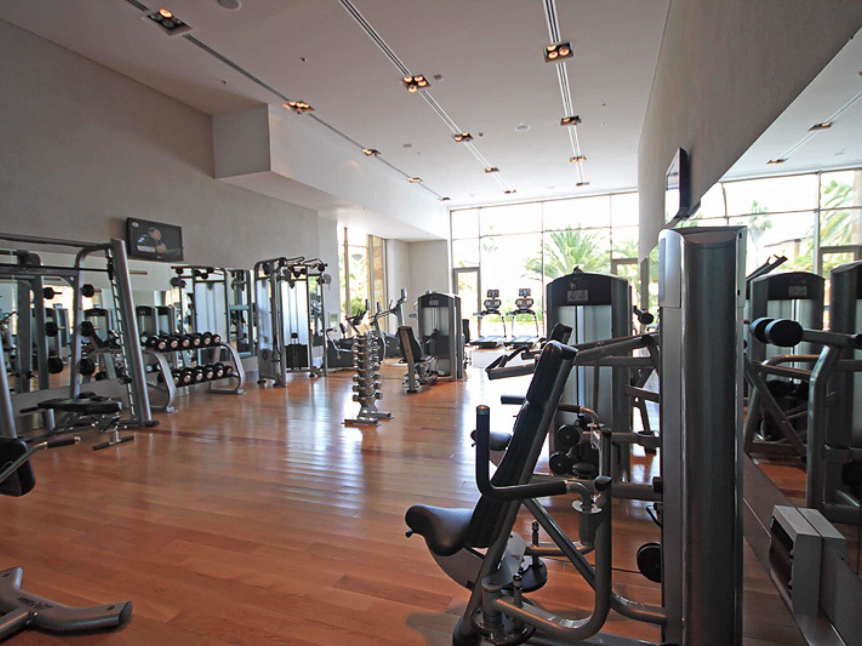A spacious gym with various exercise equipment, large mirrors, and a wooden floor.