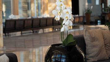 Un moderno vestíbulo con un jarrón negro de orquídeas blancas sobre una mesa de madera, un sofá con cojines y un banco al fondo.