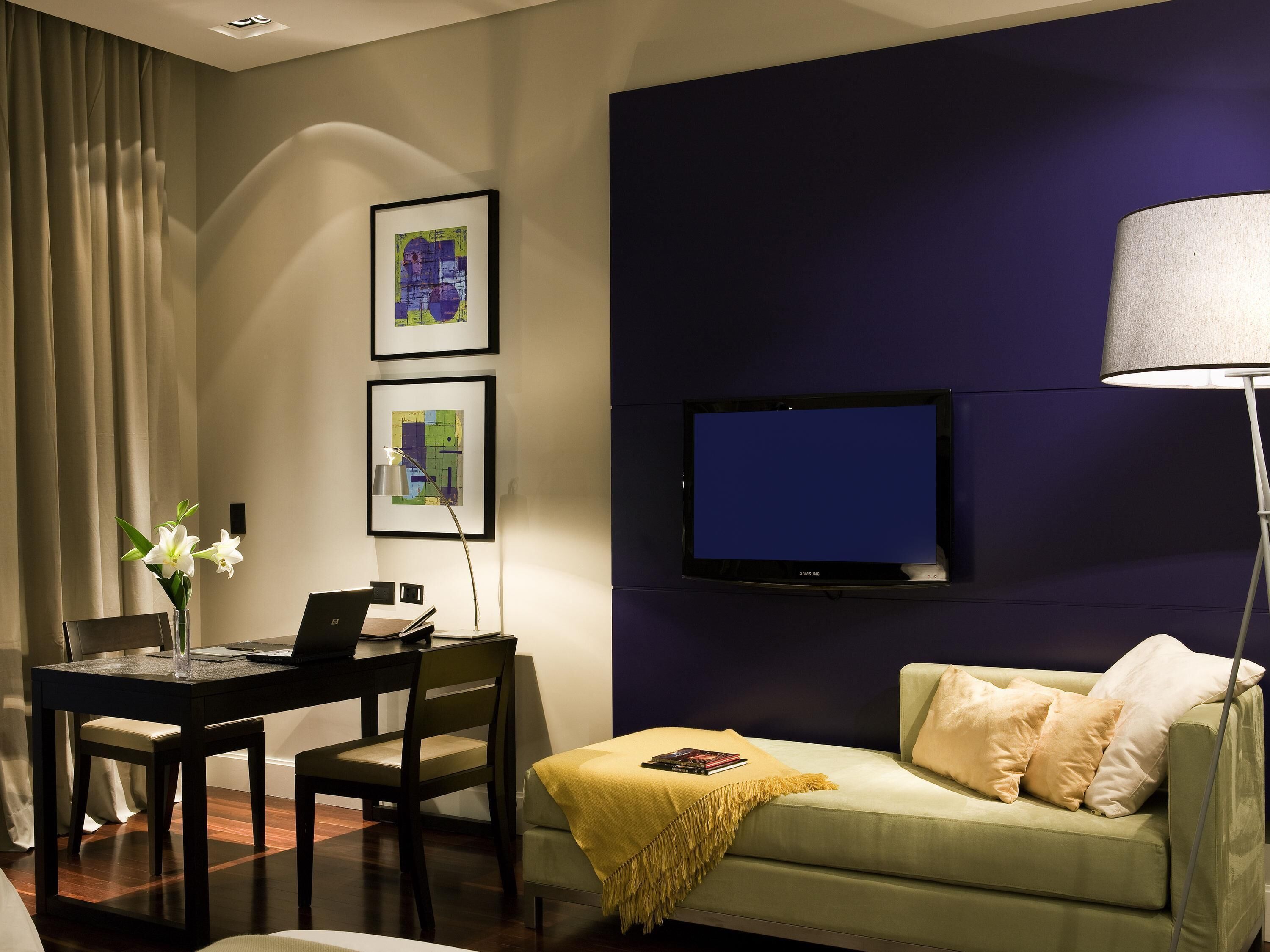 A modern living room with a flat-screen TV, a dining area with a table and chairs, and a sofa with a throw blanket.