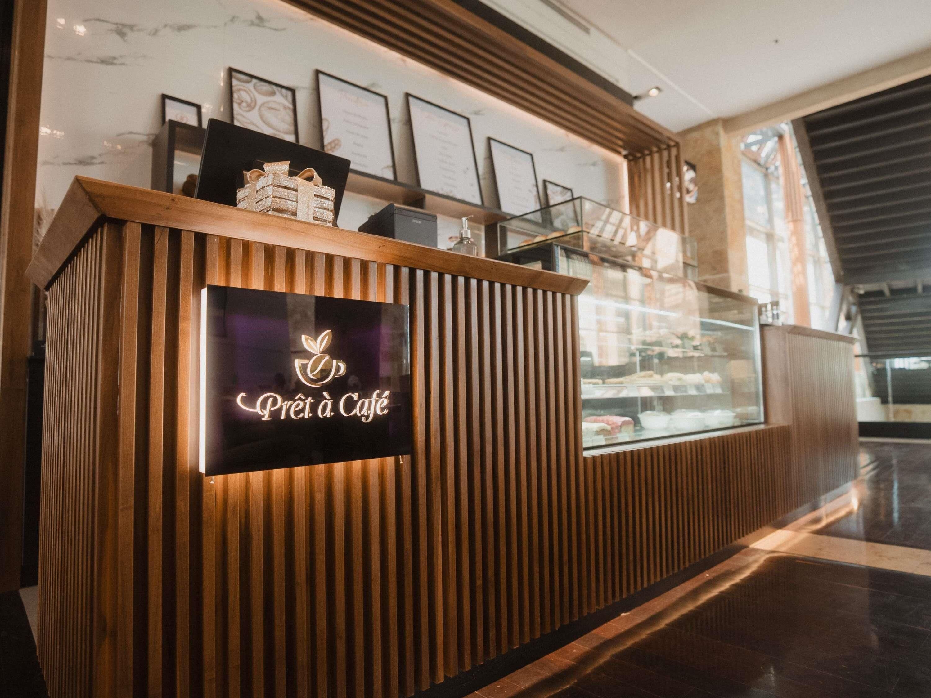 A wooden reception desk with a lit sign reading 'Prêt à Café' and framed menu items above it.