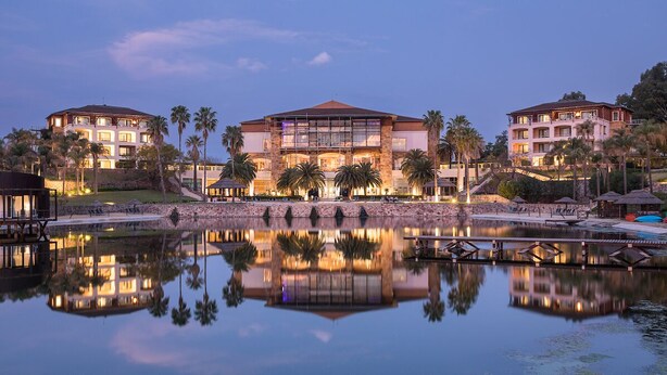 A large, multi-story hotel with a central courtyard, palm trees, and a body of water reflecting the building. - Sofitel La Reserva Cardales (Campana)