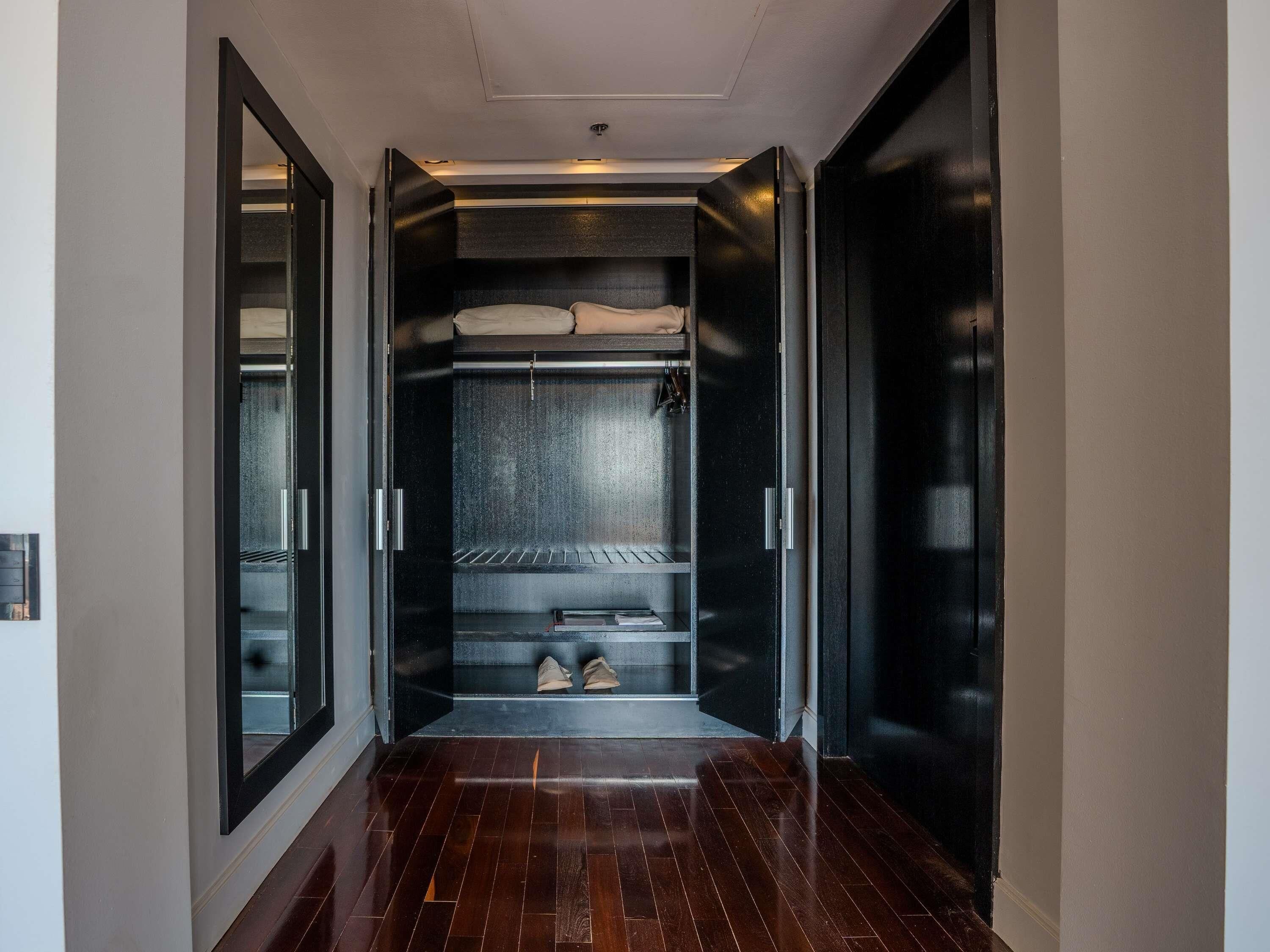 A hallway with a built-in wardrobe featuring a mirrored closet door, a shelf with shoes, and a bed with a headboard.