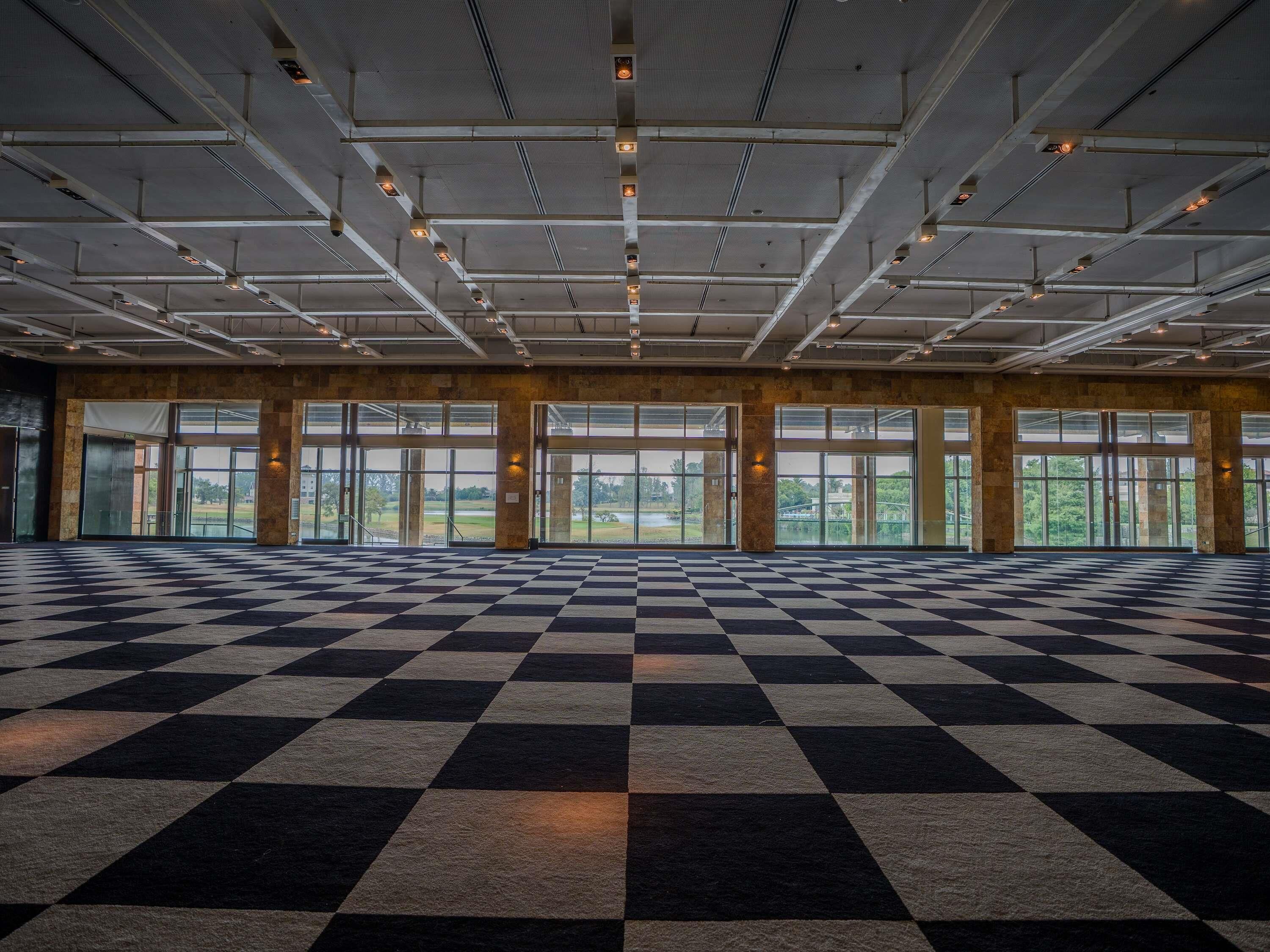 A spacious indoor area with a checkered floor, large windows, and a high ceiling with lighting fixtures.